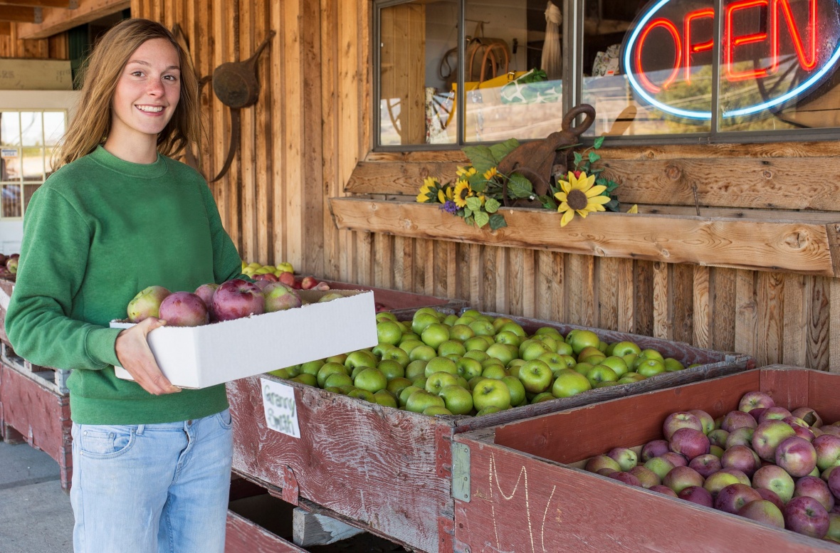 Apples at a fruit stand with a female consumer holding a box of apples